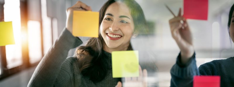 Young  businesswoman creative team using post it notes in glass wall to writing strategy business plan to development grow to success.